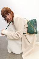 Woman holding a green handbag with gold chain strap against a white background